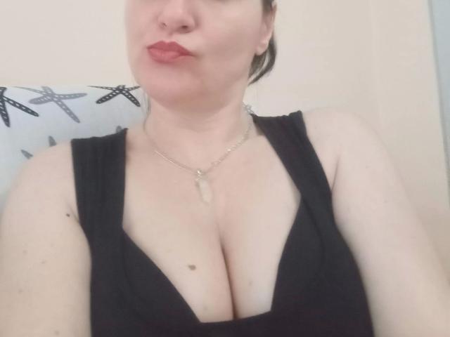 Primo piano di Monica, dall'aspetto erotico e sensuale, che mostra la sua pelle chiara e il rossetto rosso. Indossa un abito nero con scollatura profonda che mette in risalto il décolleté, e una delicata collana. Lo sfondo include linee nere astratte. Incredibilmente sexy..