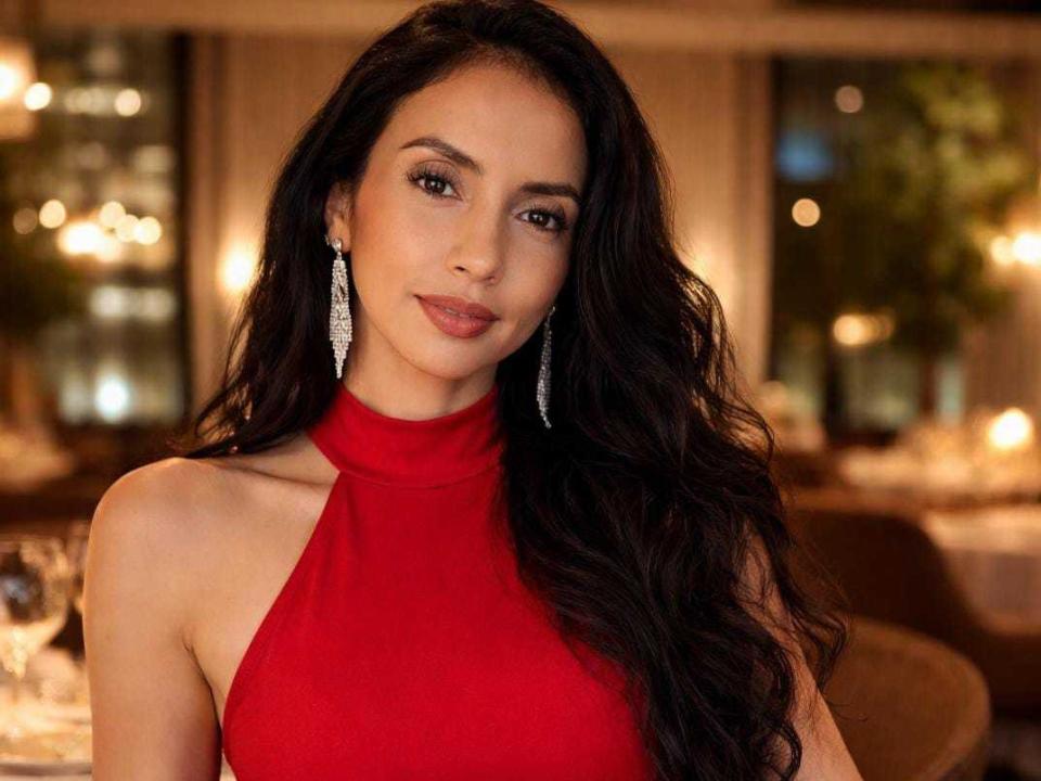 BelladonnaLips, sexy brunette with long wavy hair, wearing a red halter top, dangling earrings, soft smile, dimly lit restaurant background, blurred lights, seductive gaze, slight shadow on her right cheek.