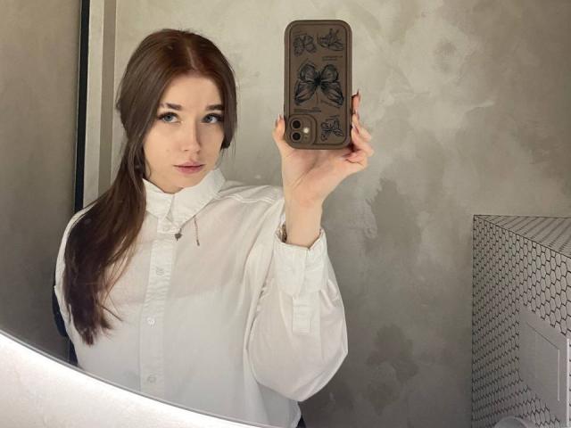 Theressa Buzzo, mit langen, dunkelbraunen Haaren, macht ein Selfie vor einem Spiegel mit ihrem Handy, das mit Schmetterlingsaufklebern verziert ist. Sie trägt ein weißes Hemd, hält das Telefon in ihrer rechten Hand und schaut direkt in die Kamera..