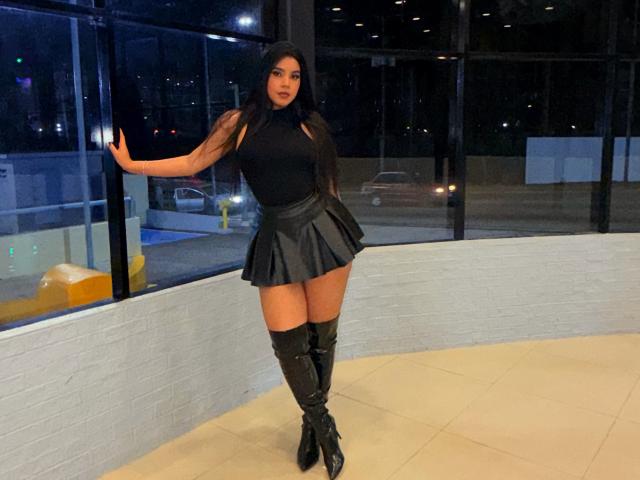 ArtemisaStone está em frente a uma parede de vidro à noite, vestindo uma blusa preta sem mangas, uma saia preta curta e meias até a coxa. Botas pretas.
ela está apoiada com uma mão na parede, pernas afastadas, com uma expressão sedutora..