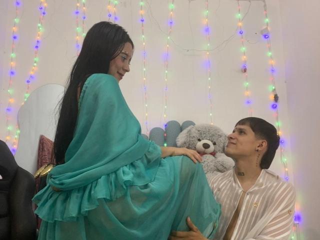 AnjaliRohan, met lang zwart haar, draagt een turquoise sjaal, zit op schoot bij een man, en houdt een grijze teddybeer vast, kleurrijk. Lichtjes in de achtergrond, informeel, aantrekkelijk, intieme sfeer..