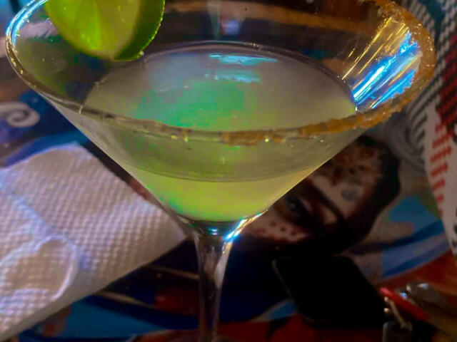 Gros plan d'un cocktail avec un quartier de citron vert sur le bord, un liquide vert et une croûte de sucre. Verre brillant, arrière-plan flou. Surface réfléchissante, couleurs vives. Boisson incroyablement séduisante..