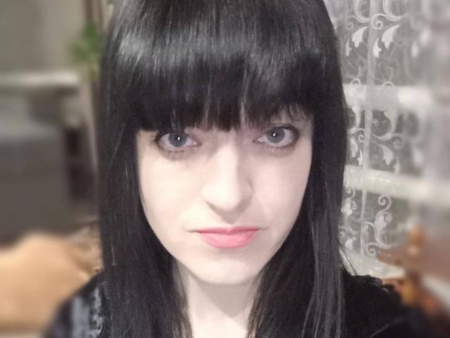 Close-up of Liliit with pale skin, black straight hair, and bangs, intense blue eyes, and pink lips. She gazes directly at the camera, creating a sense of sexual tension.