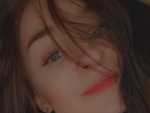 Close-up of Lilit69's face, with messy brown hair covering one eye, blue eyes, red lipstick, and a nose piercing. Her expression is slightly sultry, creating a sexual tension vibe.