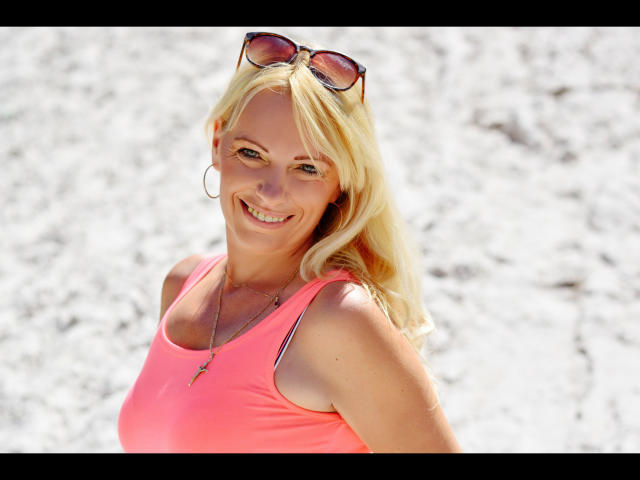 Mujer rubia, SofieHot-sex, camiseta rosa brillante, sonriendo, gafas de sol en la cabeza, fondo blanco, luz solar resaltando. cabello, informal, sexy, ligera sombra debajo del mentón, ambiente veraniego, confianza, pose relajada..