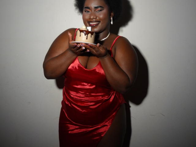 Foto van Dilay, een mollige zwarte vrouw met donkere huid en een kort afro, die een glanzende rode satijnen jurk draagt en een taart vasthoudt. met druipende chocolade, stralend van opwinding.