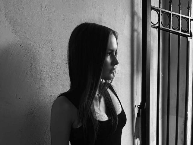 Schwarz-weißes Foto von HyoRiopel, die neben einem vergitterten Fenster steht, Profilaufnahme, Gesicht im Schatten, langes Haar, trägt ein tanktop, das ein weiches Licht wirft und dramatische Schatten erzeugt, eine intensive und stimmungsvolle Atmosphäre..