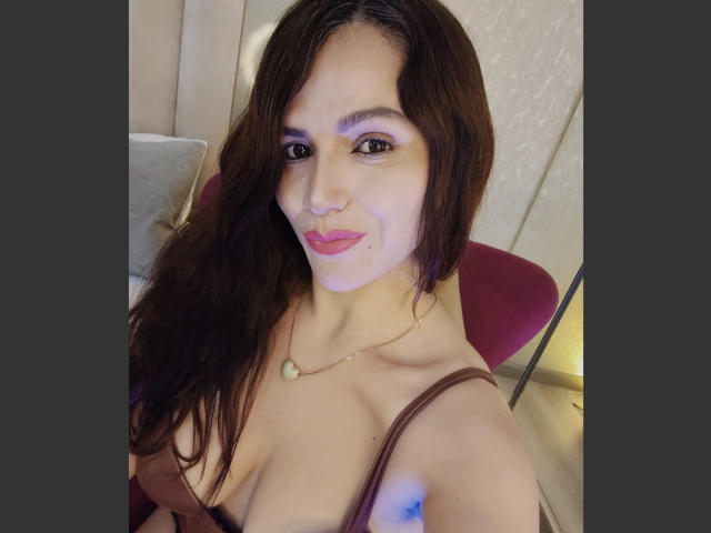 Fotografia di CameronViviane con lunghi capelli castani, incarnato medio, che indossa una maglia marrone scollata, una collana dorata e rossetto rosa.
sorride, guardando la fotocamera con un'aria sexy e sicura di sé..