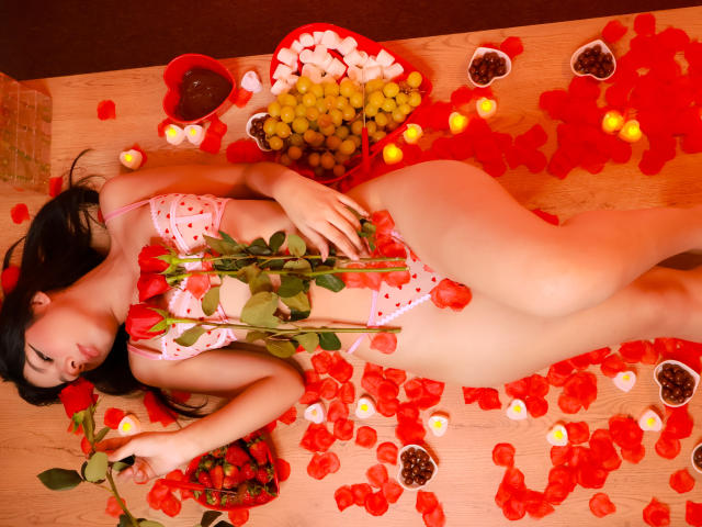 ZoeWinfrey lies on a wooden surface, nude except for a white lace bra, surrounded by red rose petals, cherry halves, and grapes. Her hand rests on her stomach, eyes closed. Fucking sexy.