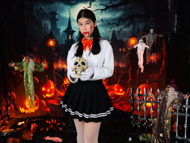 Digital artwork of ZoeWinfrey in a white blouse and black skirt, holding a skull, surrounded by Halloween decorations, glowing jack-o'-lanterns, and spooky figures with bats in the background.