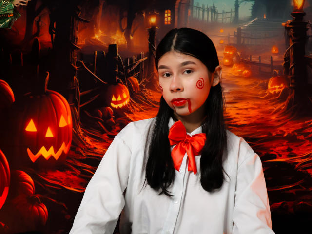 ZoeWinfrey, una mujer asiática con cabello largo y negro, lleva una camisa blanca y una corbata roja, con la cara pintada con remolinos rojos. rodeado de calabazas iluminadas en un ambiente oscuro y festivo de Halloween..