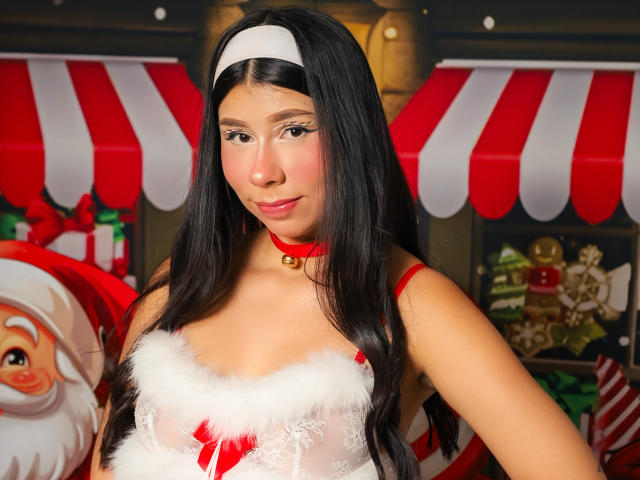 Zoe Winfrey, avec de longs cheveux noirs, un bandeau blanc et un collier rouge, portant un haut en dentelle blanche et rouge. Visage du Père Noël sur la gauche, avec un auvent rayé rouge et blanc en arrière-plan. Tension sexuelle.