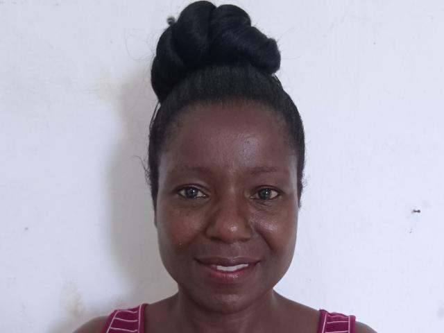 Photograph of a dark-skinned woman with a high bun, smiling slightly, wearing a red and white striped top. Her face has visible pores, and there's a small red mark on her cheek.