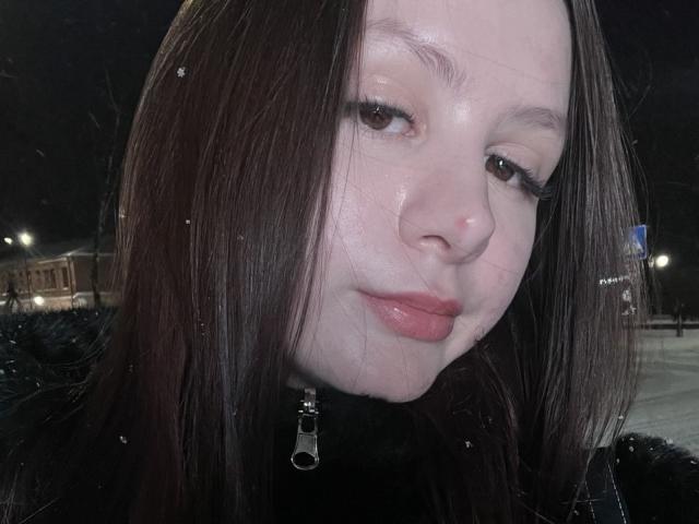 Close-up van LaylaArchibeque, bleke huid, glanzend gezicht, donkerbruin haar, lichte grijns, draagt een zwarte jas met zilver. rits, nachtelijke straatachtergrond, gedimd licht, natte uitstraling, seksuele spanning, suggestieve sfeer..