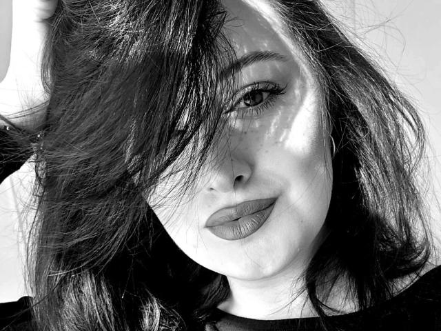 Black and white photo of KlaraxGold, face partially obscured by dark, messy hair, intense gaze, full lips slightly parted, stark shadows on face, high contrast, intense sexual tension, moody lighting.