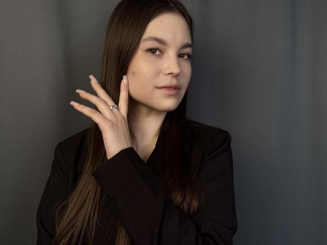 Photograph of TerrilynDeprospero, a sexy woman with long dark hair, pale skin, and a subtle mole on her cheek. She's wearing a black top, holding her hand up, with a seductive look.