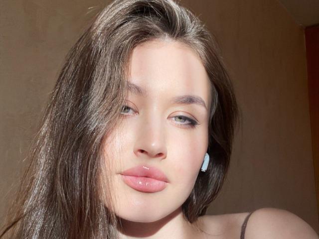 Close-up van EstherDambrose, lichtgetint met glanzende, roze lippen, donkerbruin haar, zonlicht accentueert het gezicht, zacht schaduwen, lichtblauwe oorbellen, intense blik, subtiele seksuele spanning, natuurlijk licht, lichtrode huid..