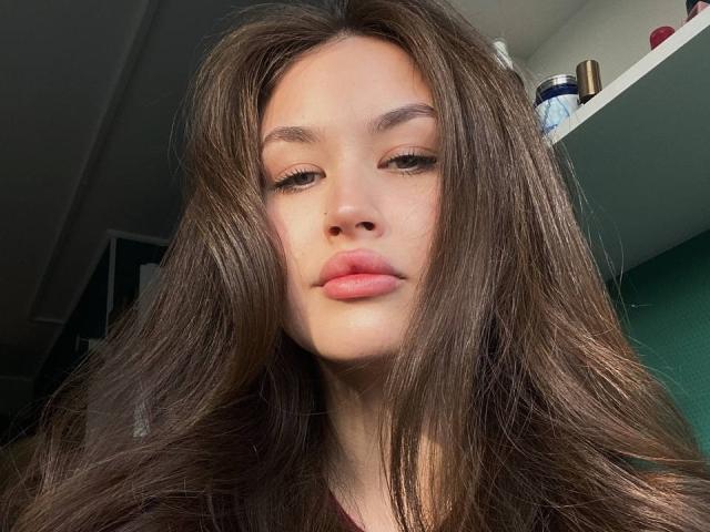 Fotografía de primer plano de EstherDambrose, una joven con cabello largo y castaño oscuro, piel pálida y labios carnosos. Tiene una expresión relajada, una mirada directa y un sombreado sutil. Increíblemente atractivo/a..