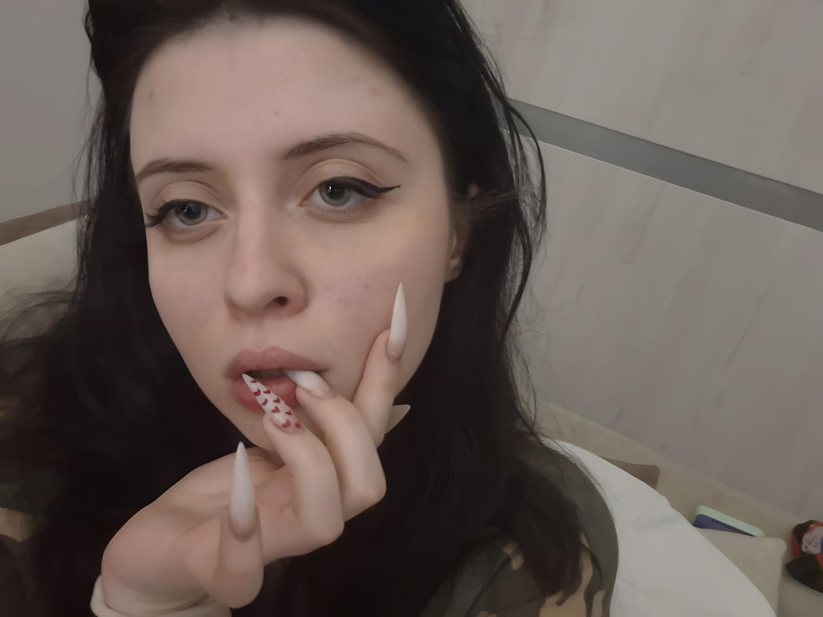 Close-up van DanielleZiego, met bleke huid, donker haar, blauwe ogen en lange witte nagels, die aan een rode en witte een lolly met een patroon, die recht in de camera kijkt met een licht geopende mond..