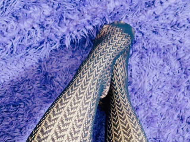 Gros plan de deux jambes entrelacées, ornées de motifs, avec une texture bleue et duveteuse en arrière-plan. Les pieds présentent un motif en zigzag, créant un aspect sensuel et entrelacé. La scène est chargée de tension sexuelle..