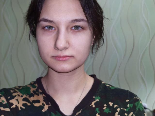 Fotografía de primer plano de Filomena Stotelmyer, con piel pálida, cabello oscuro y una expresión neutra. Ella lleva una camisa de camuflaje y un collar delgado. Fondo ondulado de color verde claro. Mirada muy seria..