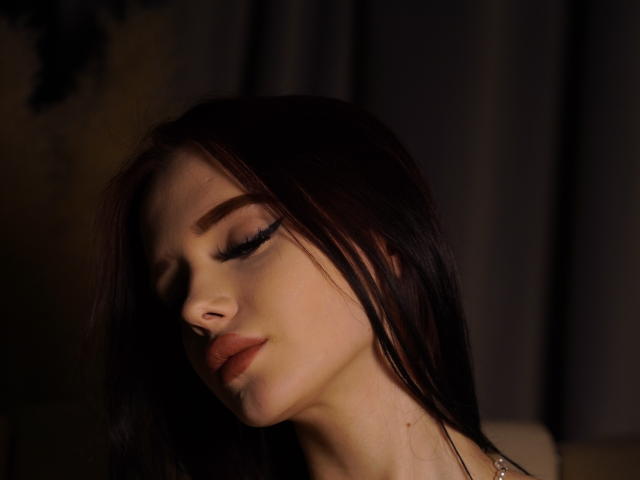 AleneNghiem heeft donkerbruin haar, gesloten ogen met lange wimpers en lichtroze lippen die iets open zijn. Zacht licht accentueert haar bleke huid en delicate gelaatstrekken..