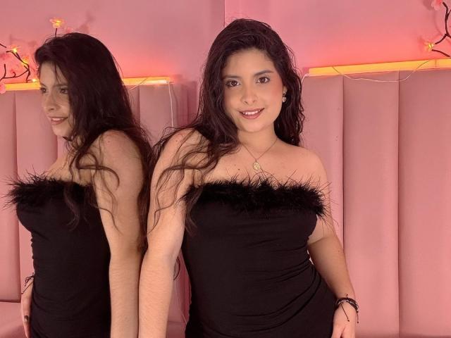 Luciana Blake, uma mulher curvilínea com longos cabelos pretos, está em frente a uma parede rosa e acolchoada. Ela veste um vestido preto sem alças, com detalhes de pele, e sorri com confiança. Seu reflexo é visível. As luzes de neon projetam um brilho rosa..