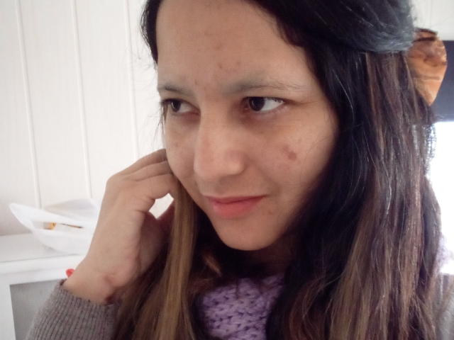 Close-up photo of Dafbe with long brown hair, light skin, and a few acne spots. She's looking to the side, touching her cheek with a hand. Wearing a purple knit scarf. Fucking sexy.