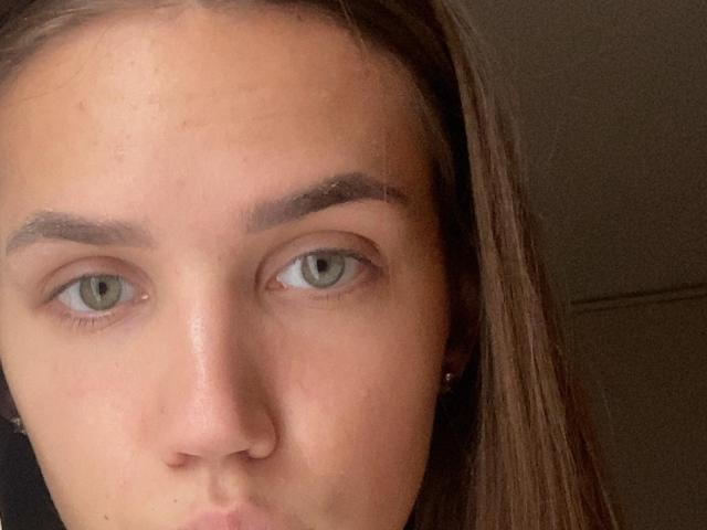 Close-up foto van het gezicht van MartiWamble, met groene ogen, licht open lippen en bruin haar. De uitdrukking van MartiWamble is neutraal, met zichtbare huidtextuur. De afbeelding heeft een erotische sfeer..