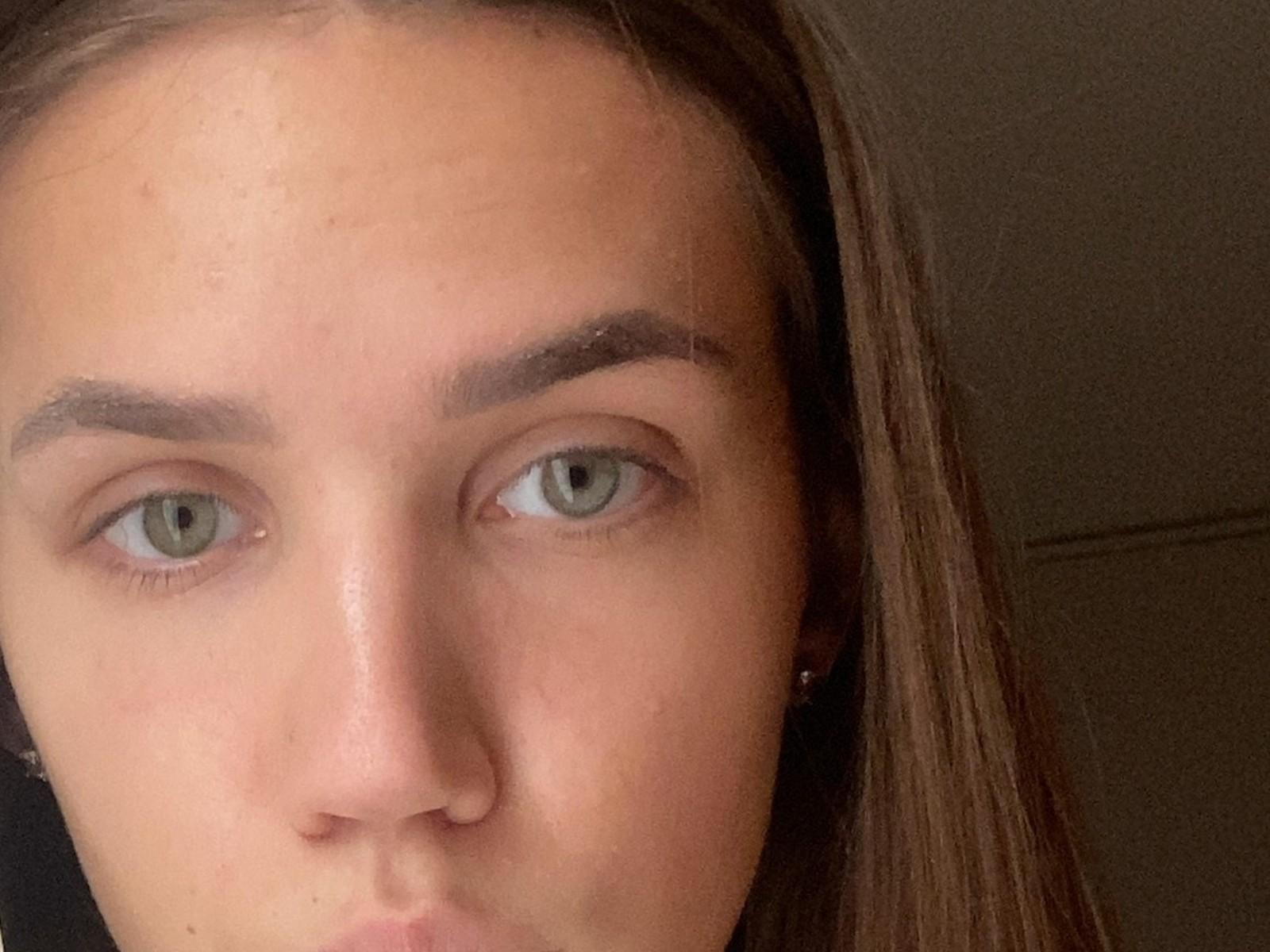 Nahaufnahme von MartiWambles Gesicht mit grünen Augen, leicht geöffneten Lippen und braunen Haaren. Der Gesichtsausdruck von MartiWamble ist neutral, wobei die Hautstruktur sichtbar ist. Das Bild hat eine sexuell aufgeladene Atmosphäre..