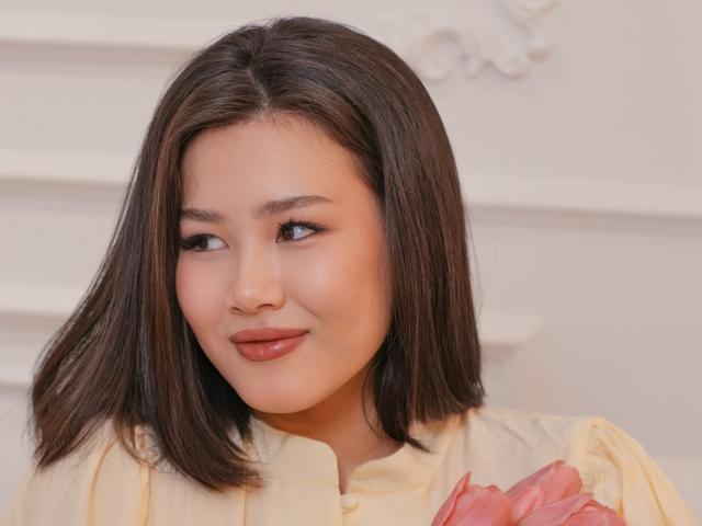 Close-up de ArianaFlower, uma mulher asiática com cabelo preto liso, pele clara e batom vermelho, vestindo uma blusa creme. Com detalhes florais em tons de rosa, olhando ligeiramente para o lado com um sorriso discreto..