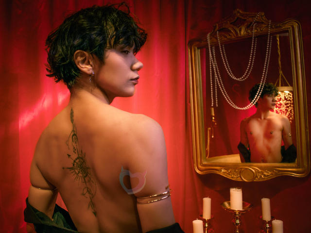 EriolWest, torse nu, avec des cheveux noirs courts, un tatouage sur le dos, un bracelet en or, un fond de rideau rouge, un miroir qui se reflète. La poitrine d'EriolWest, des bougies, un collier de perles, un éclairage rouge intense, une tension sexuelle, une pose séduisante..