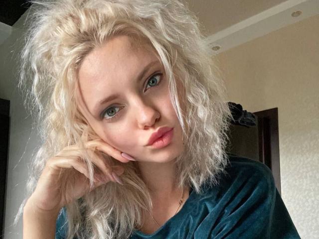 Close-up photo of CrystalHope, a blonde woman with messy hair, blue eyes, and pink lips, looking directly at the camera with a slightly pouty expression. She's wearing a black shirt.