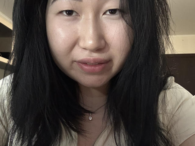 Photo en gros plan de TeriMceady, avec de longs cheveux noirs, une peau claire et des lèvres légèrement entrouvertes. Elle porte une chemise blanche avec un collier orné d'un pendentif. Ses yeux sont fixés directement sur l'appareil photo, créant un regard direct et intense..