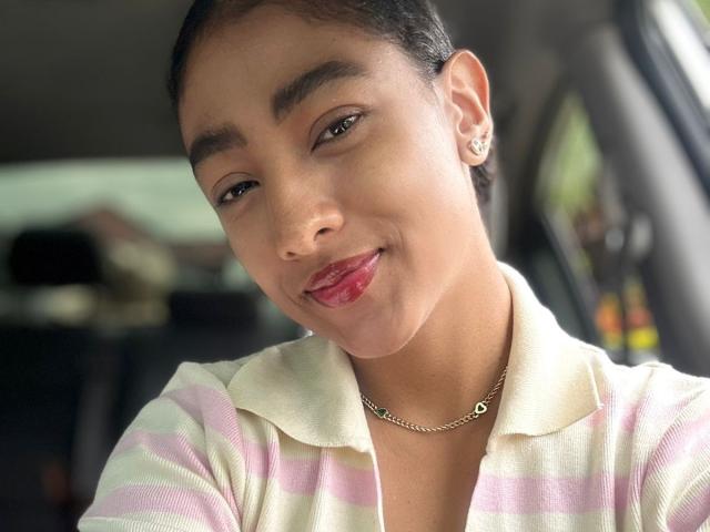 Close-up of NatalyBlonder, medium skin tone, short black hair, red lipstick, white collared shirt, gold necklace, slight smile, cock in mind, visible earrings, natural light, soft focus, car interior.