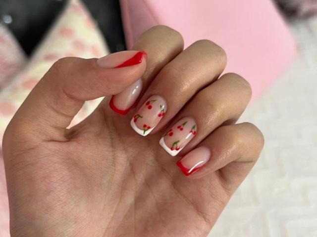 Close-up of IsabellaJames's hand with glossy red and white nail art, featuring small red dots on each nail. The nails are shaped square with red tips. Skin is smooth, light-toned.