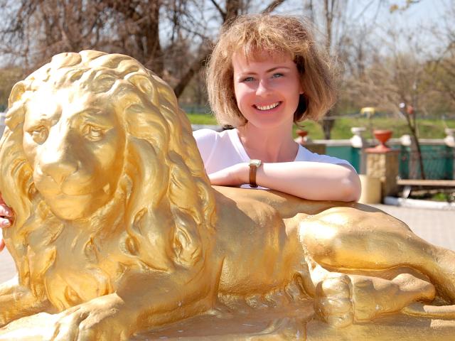 SunnySoul-hot leunt tegen een helder gouden leeuwenbeeld, met een glimlach en kort bruin haar. De gedetailleerde manen van de leeuw contrasteren met het witte shirt van SunnySoul-hot. De ontspannen houding van SunnySoul-hot straalt een nonchalante zelfverzekerdheid uit..