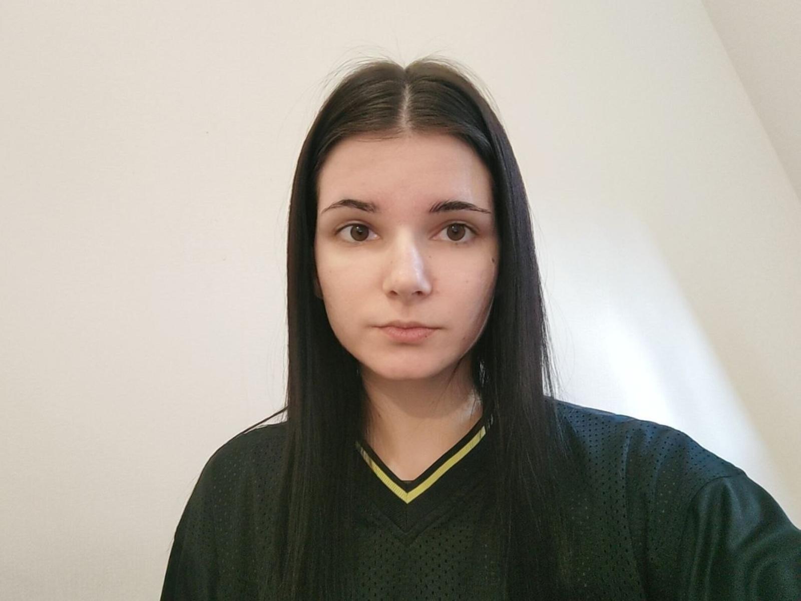 Fotografia de Sigrid Iniestra com cabelo preto liso, pele clara e olhos castanhos, vestindo uma camisa preta com decote em V. Ela está centralizada, olhando diretamente para a câmera, com uma expressão neutra. Muito sério..