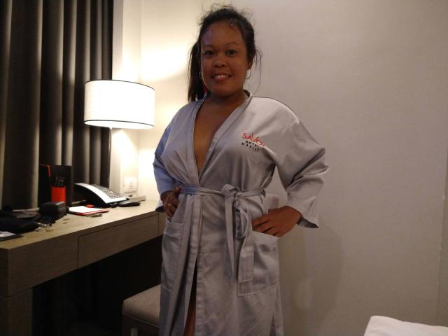 Filipina69-hot está em um quarto com pouca luz, vestindo um roupão de cetim branco com um logotipo vermelho no peito, com as mãos nos quadris. sorrindo.
luminária e cortinas escuras ao fundo.