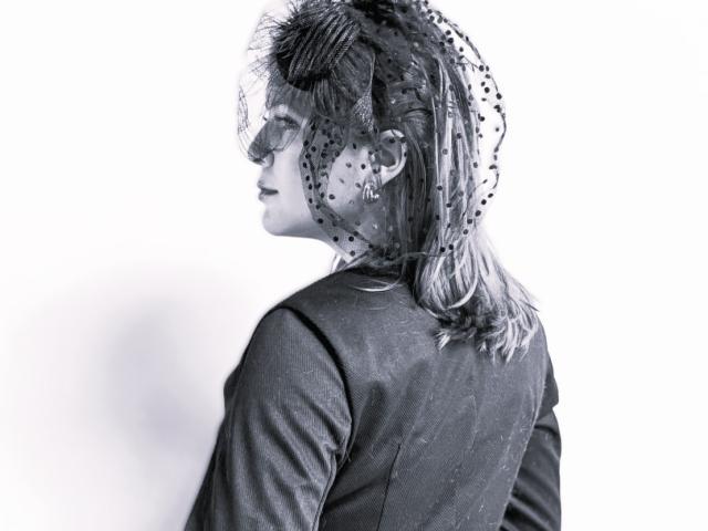 Fotografia em preto e branco de MoonXVelvet com o cabelo despenteado, vestindo uma jaqueta escura e texturizada. Perfil lateral, olhando para a esquerda. Faixa de cabeça com bolinhas, luz vindo da direita, sombra no lado esquerdo. Muito atraente..