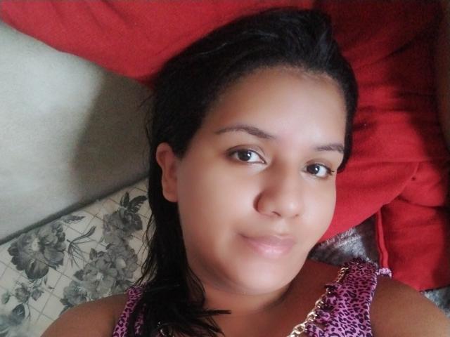 Daybb has medium brown skin, black hair, and is wearing a purple leopard print top. She's smiling slightly with brown eyes, looking at the camera. Her tits are small.