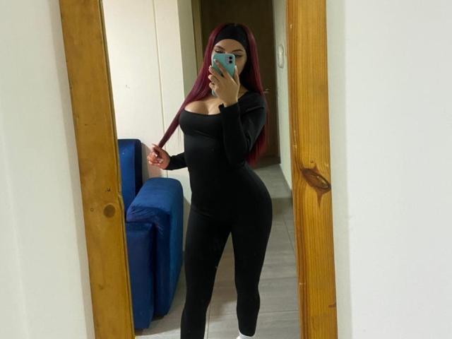 ValeryHarllow takes a mirror selfie, wearing a tight black off-shoulder bodysuit that accentuates her large breasts and curvy hips. She has long red hair and holds a phone, partially obscuring her face.