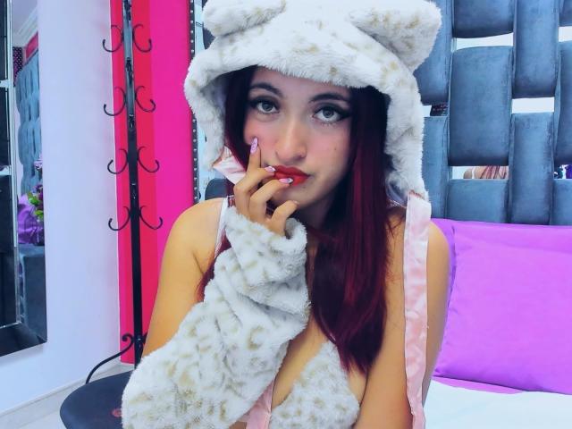 ZoeDubois, wearing a white furry bear hat and matching gloves, bites her finger seductively with red lips, dark eyes, and long brown hair. Background includes purple and red accents.