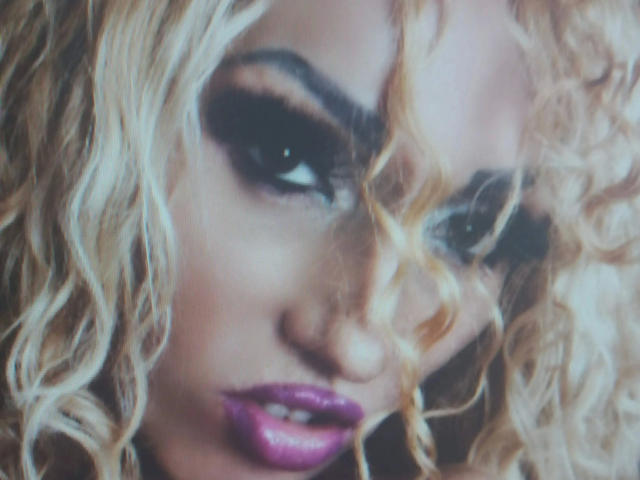 Close-up van Barbie Ballerina, met platinablond, krullend haar, dikke zwarte eyeliner en donkerpaarse lippenstift. Haar intense blik en licht geopende lippen creëren een seksuele spanning. Gerichte, prikkelende expressie.