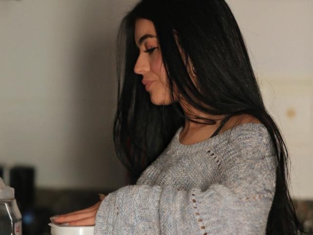 TrinityPrestige, avec de longs cheveux noirs, vue de profil, portant un pull gris à une épaule, concentrée sur une machine à café, éclairage doux, ombres subtiles, sensuel, calme, décontracté, moment intime.