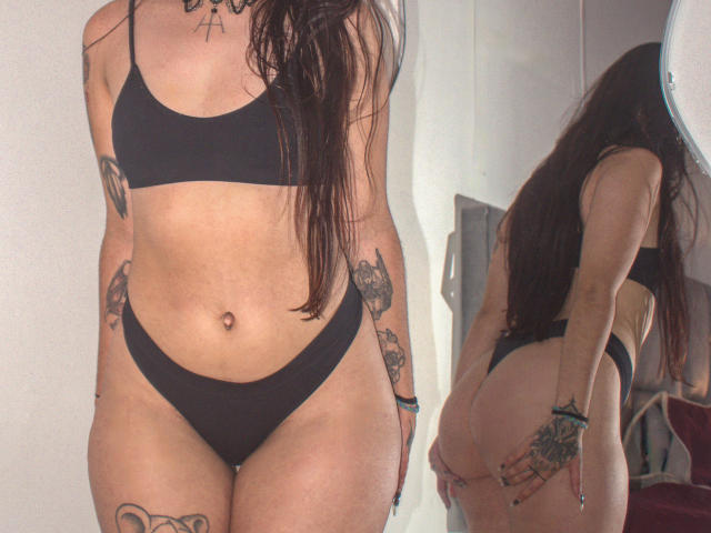 Photographie d'Helena Morningstar avec de longs cheveux bruns, portant un soutien-gorge et une culotte noirs, montrant des tatouages sur les bras et le bas du corps. abdomen. Vue de face et de dos, mettant l'accent sur son corps voluptueux et tatoué, tenant ses fesses..