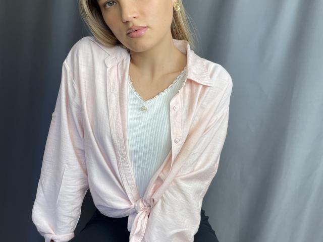 Foto em close-up de JamilaRomeiro, com pele clara, vestindo uma blusa branca amarrada na cintura, revelando uma blusa de renda branca. embaixo.
seus lábios estão ligeiramente entreabertos, transmitindo uma tensão sexual..