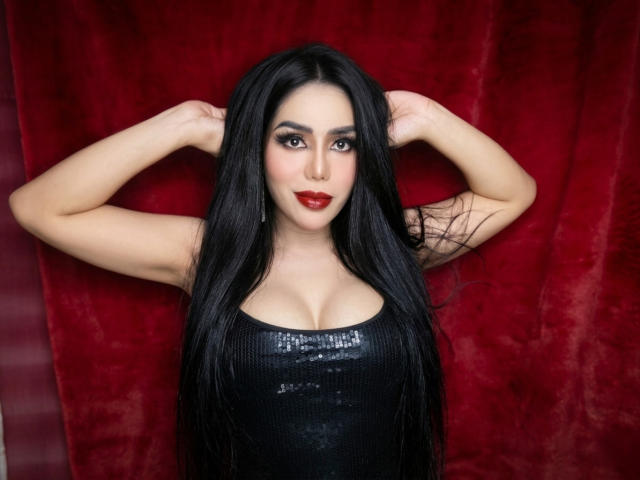 DivineMillion with long black hair, red lipstick, and a black sequined top, arms raised behind head, pale skin, intense gaze, red velvet background, sexy, seductive pose, digital art.