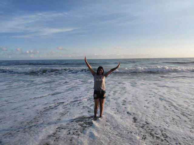 PauletteLoveX stands waist-deep in the ocean, arms raised in triumph. She's wearing a gray shirt and dark shorts, with wet, sandy legs. Waves crash around her, sky overhead. Fucking exhilarating.