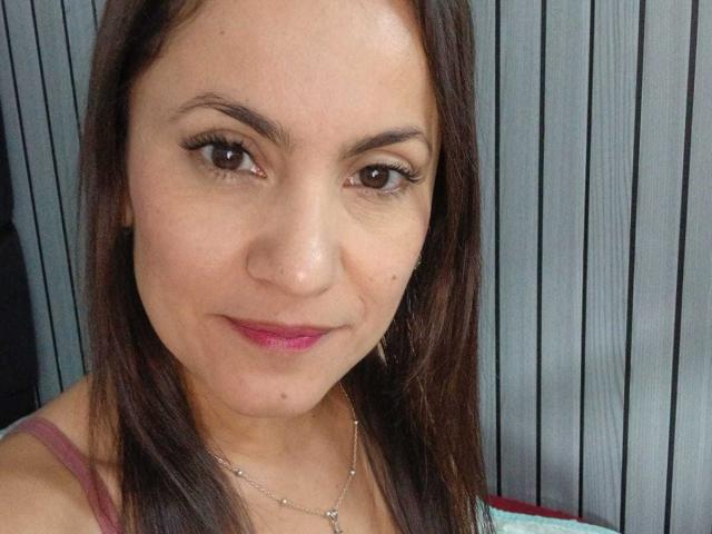 Close-up de SolaraDubois, uma jovem com cabelo castanho liso, pele clara e olhos castanhos. Ela está vestindo uma camiseta vermelha, sorri discretamente e tem uma leve tensão sexual no olhar..